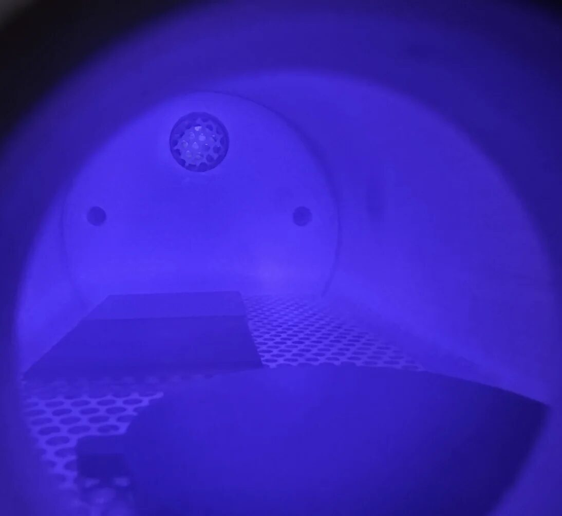 Blue-purple illuminated atomic oxygen exposure chamber with black coating samples on a perforated tray